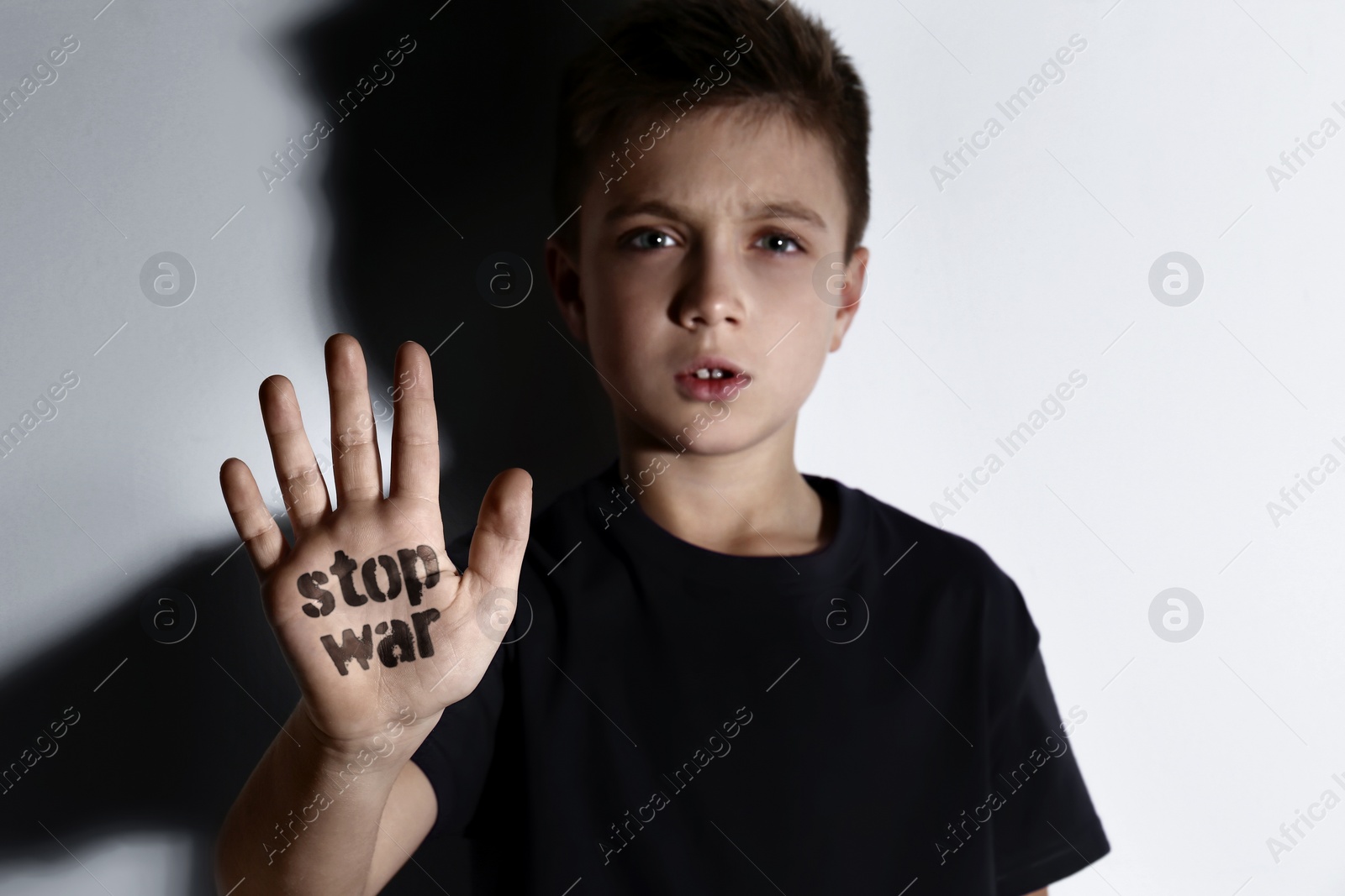 Image of Unhappy little boy showing palm with phrase Stop War near white wall