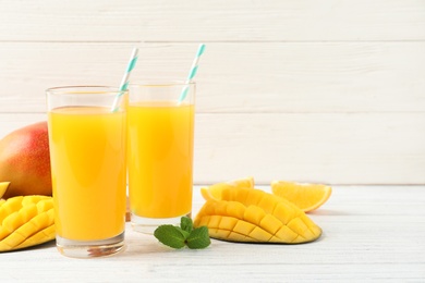 Photo of Tasty mango drink and fresh fruits on wooden table against light background. Space for text