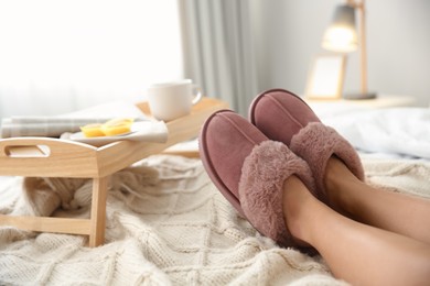 Photo of Woman wearing soft comfortable slippers on bed at home, closeup