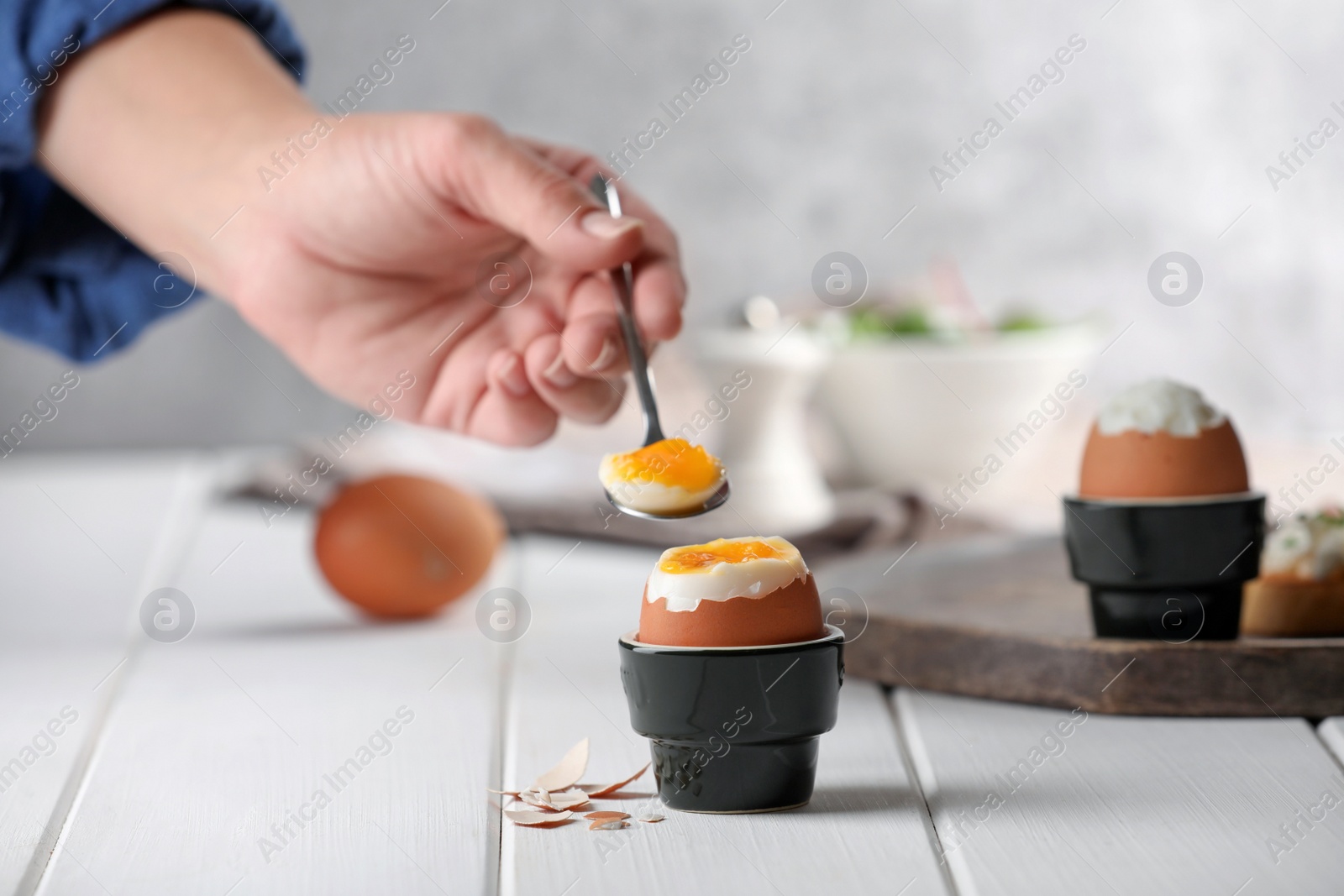 Photo of Woman eating fresh soft boiled egg at white wooden table, closeup