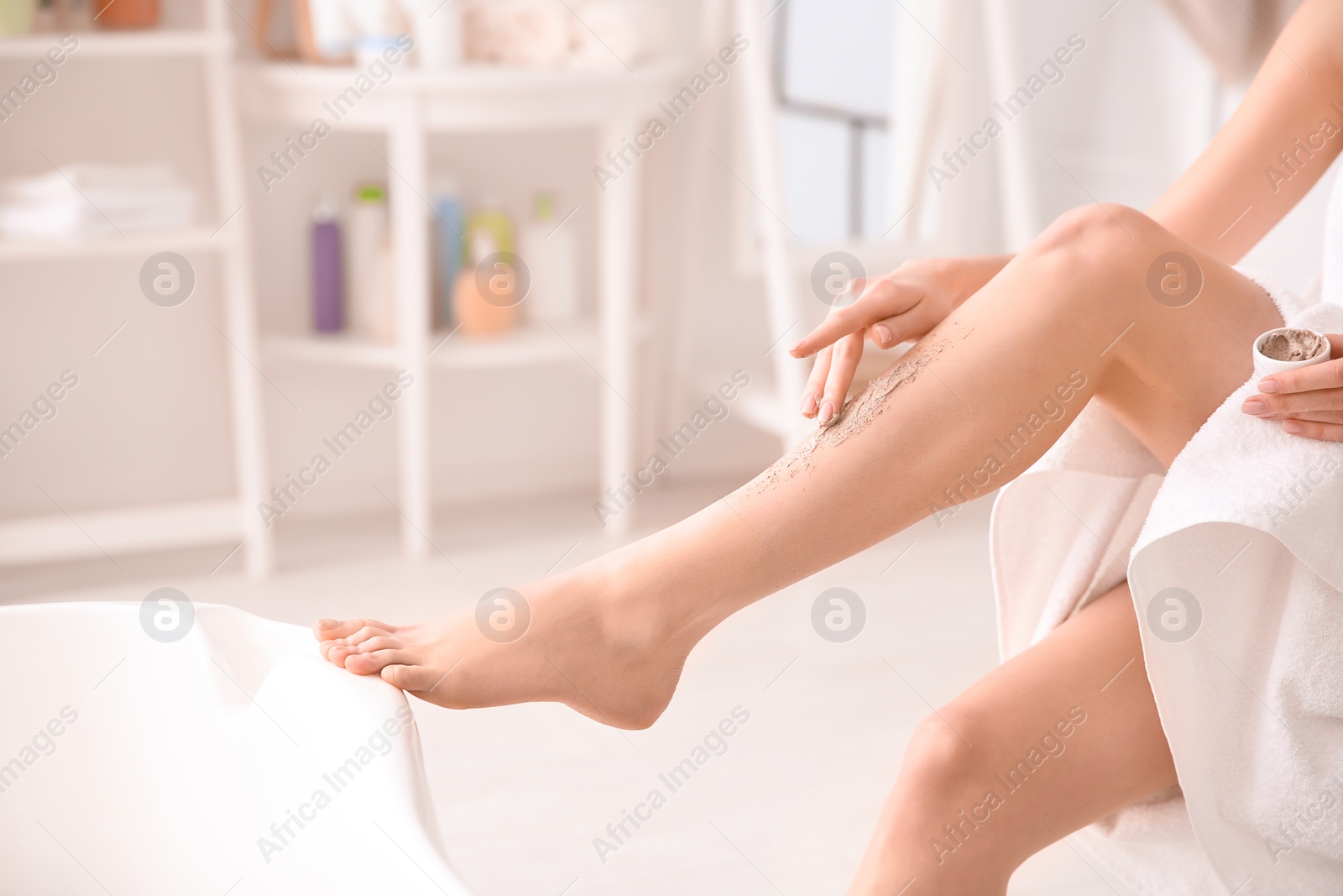 Photo of Woman applying body scrub on legs at home