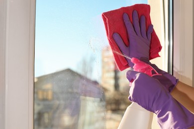 Photo of Young woman cleaning window glass with rag and detergent at home, closeup. Space for text
