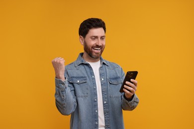 Photo of Happy man with smartphone on orange background