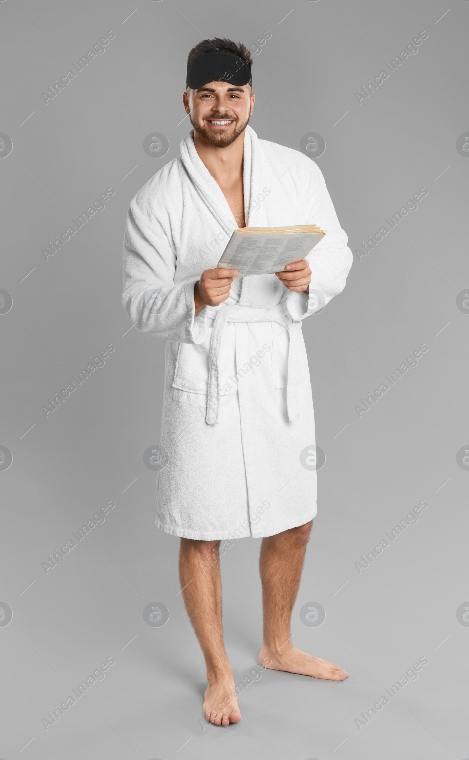 Photo of Young man in bathrobe reading newspaper on grey background