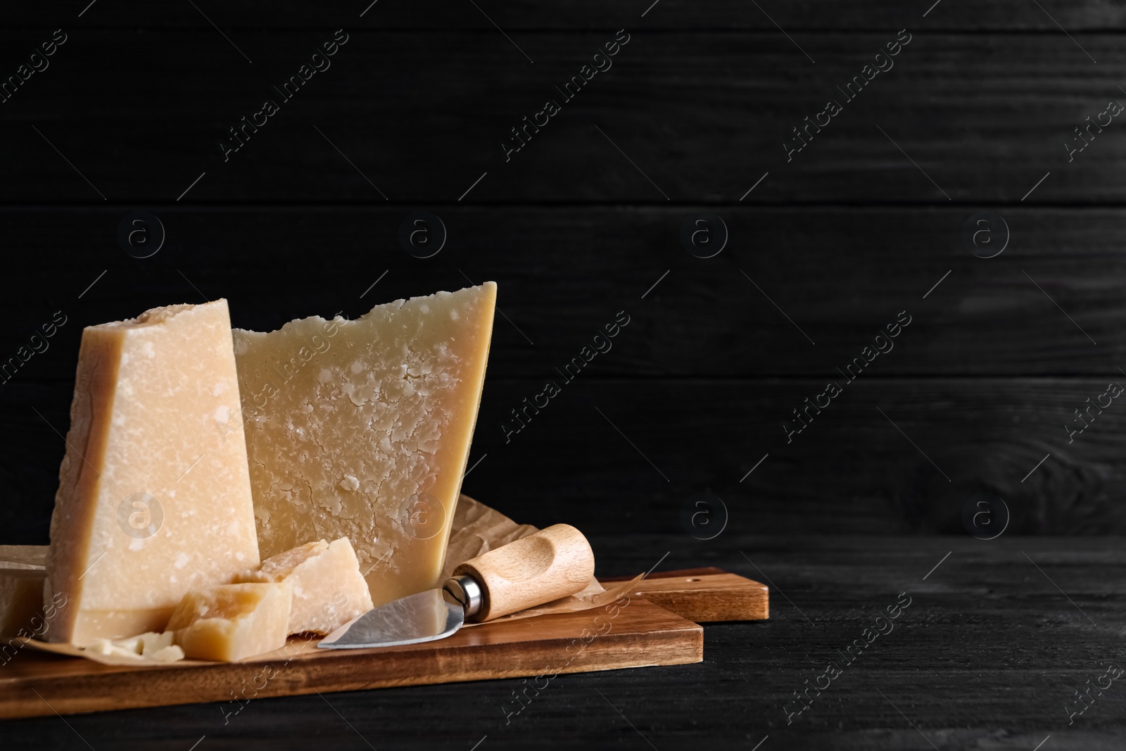 Photo of Parmesan cheese with board and knife on black wooden table. Space for text