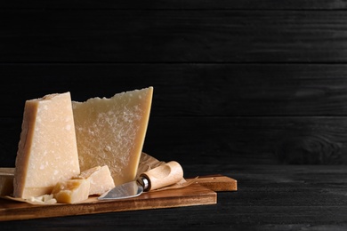 Parmesan cheese with board and knife on black wooden table. Space for text