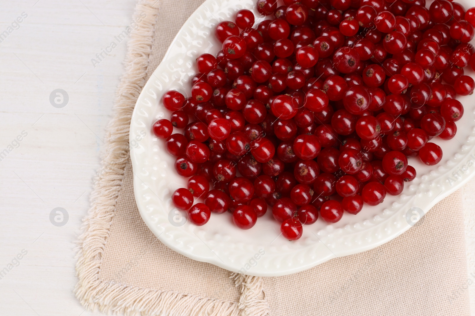 Photo of Plate with ripe red currants on white wooden table, top view