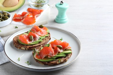 Photo of Delicious sandwiches with salmon, avocado and capers on white wooden table. Space for text