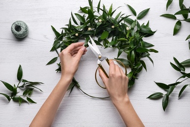 Photo of Woman making mistletoe wreath at white wooden table, top view. Traditional Christmas decor