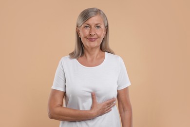 Photo of Beautiful senior woman doing breast self-examination on light brown background