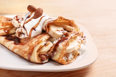 Photo of Thin pancakes served with chocolate syrup, cream and banana on plate