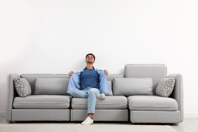 Photo of Young man relaxing on sofa against white wall