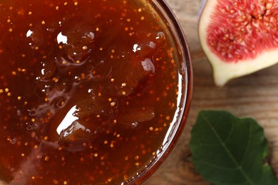 Photo of Bowl with tasty sweet jam, half of fig and leaf on wooden table, closeup