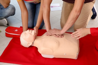 Group of people with instructor practicing CPR on mannequin at first aid class indoors, closeup