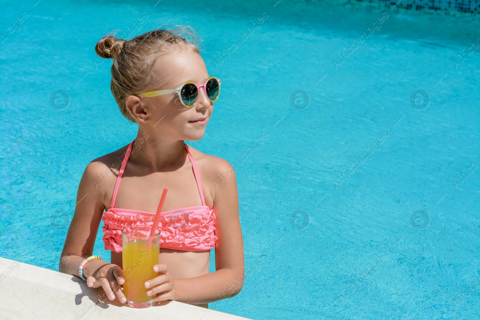 Photo of Cute little girl with glass of juice in swimming pool on sunny day. Space for text