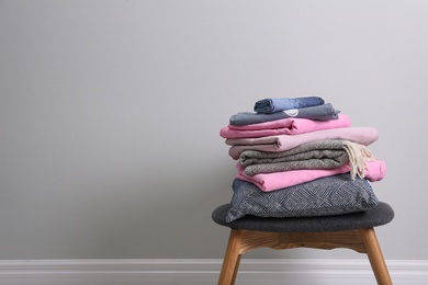 Photo of Stack of clean bed linen, plaid and pillow on stool near light grey wall. Space for text