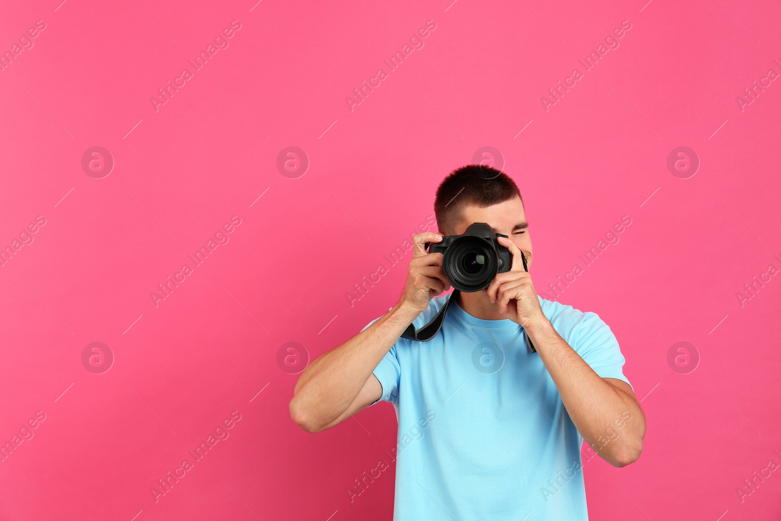 Photo of Young professional photographer taking picture on pink background. Space for text