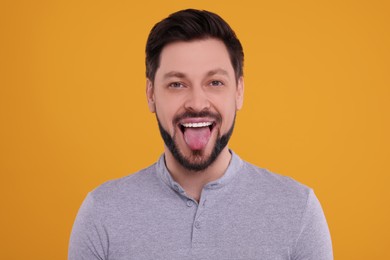 Photo of Happy man showing his tongue on orange background