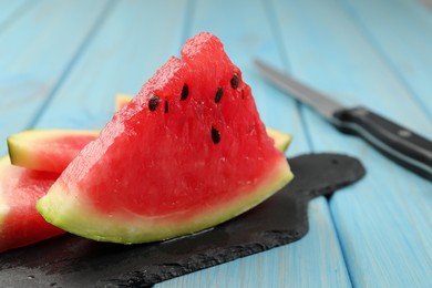 Photo of Slate board with slices of juicy watermelon on light blue wooden table, closeup