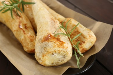 Photo of Tasty baked parsnips with rosemary on wooden table, closeup