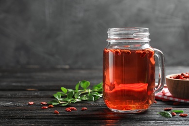 Photo of Healthy goji juice in mason jar on wooden table, space for text