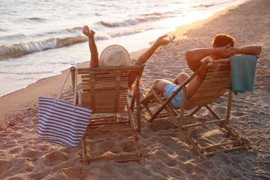 Young couple relaxing in deck chairs on beach near sea