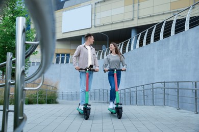 Happy couple riding modern electric kick scooters on city street