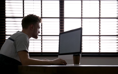 Lonely man sitting at computer with empty screen indoors