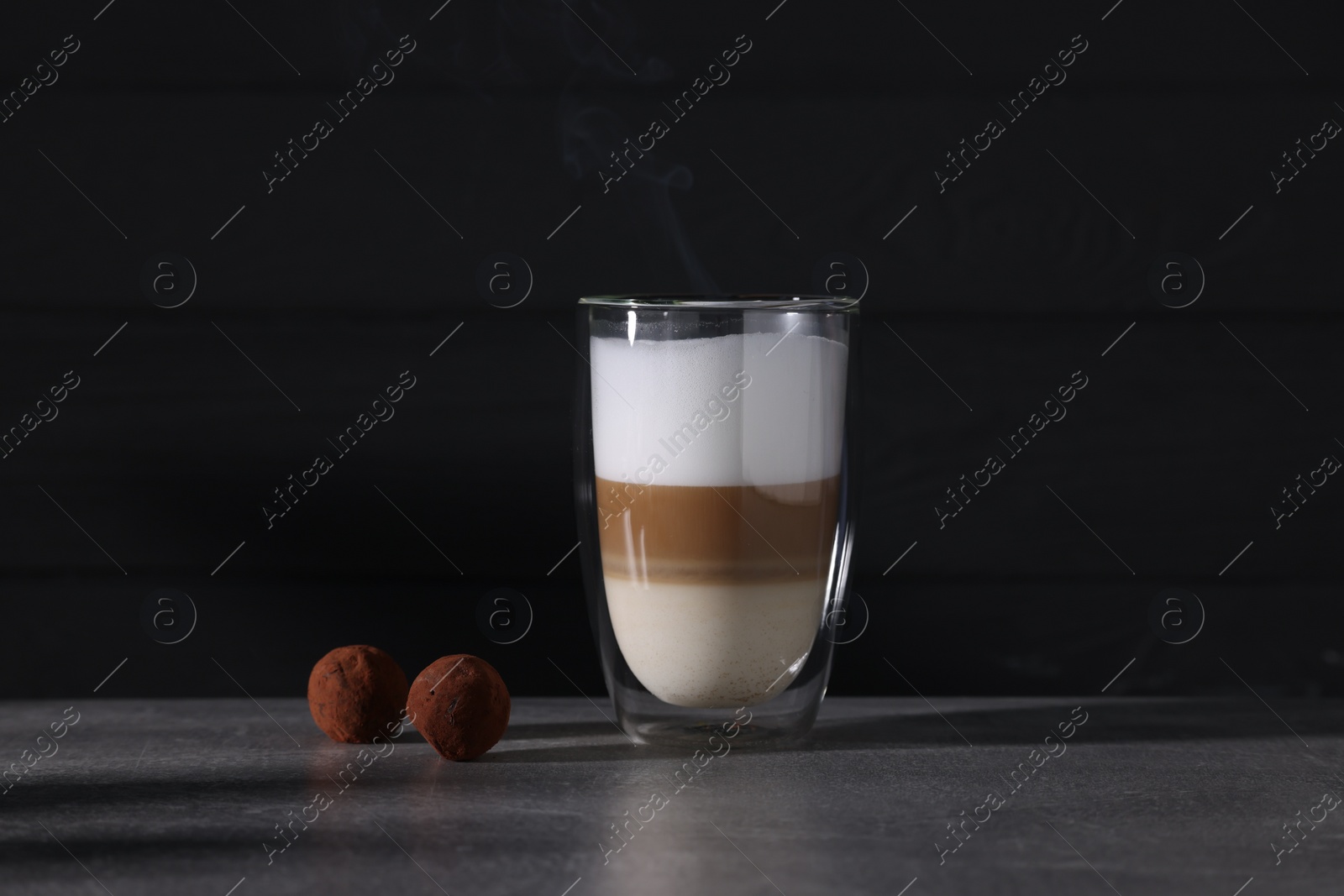 Photo of Aromatic latte macchiato in glass and chocolate candies on grey table against black background