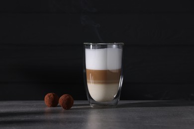 Photo of Aromatic latte macchiato in glass and chocolate candies on grey table against black background