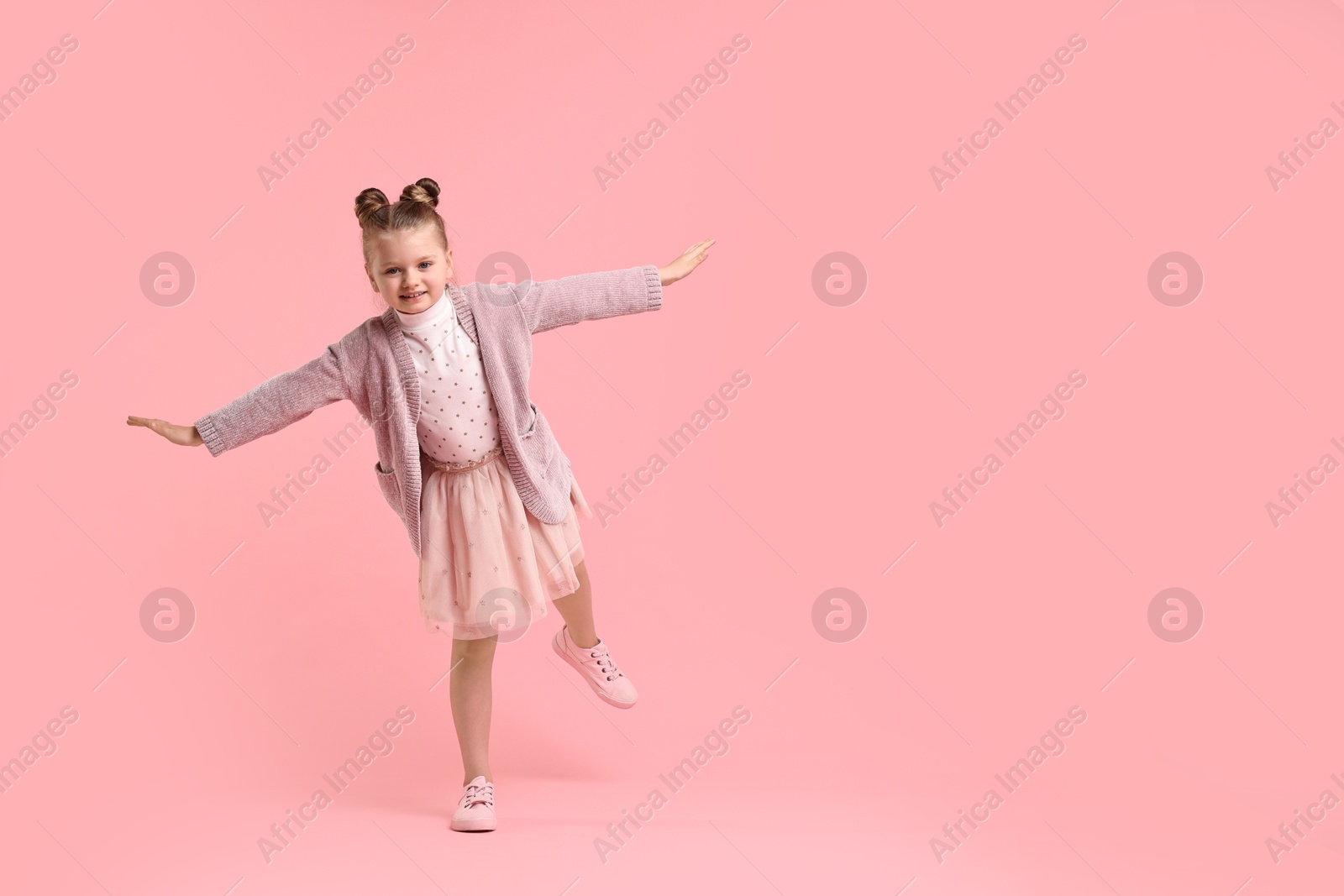 Photo of Cute little girl dancing on pink background, space for text