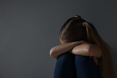 Photo of Sad girl sitting near dark grey background, space for text