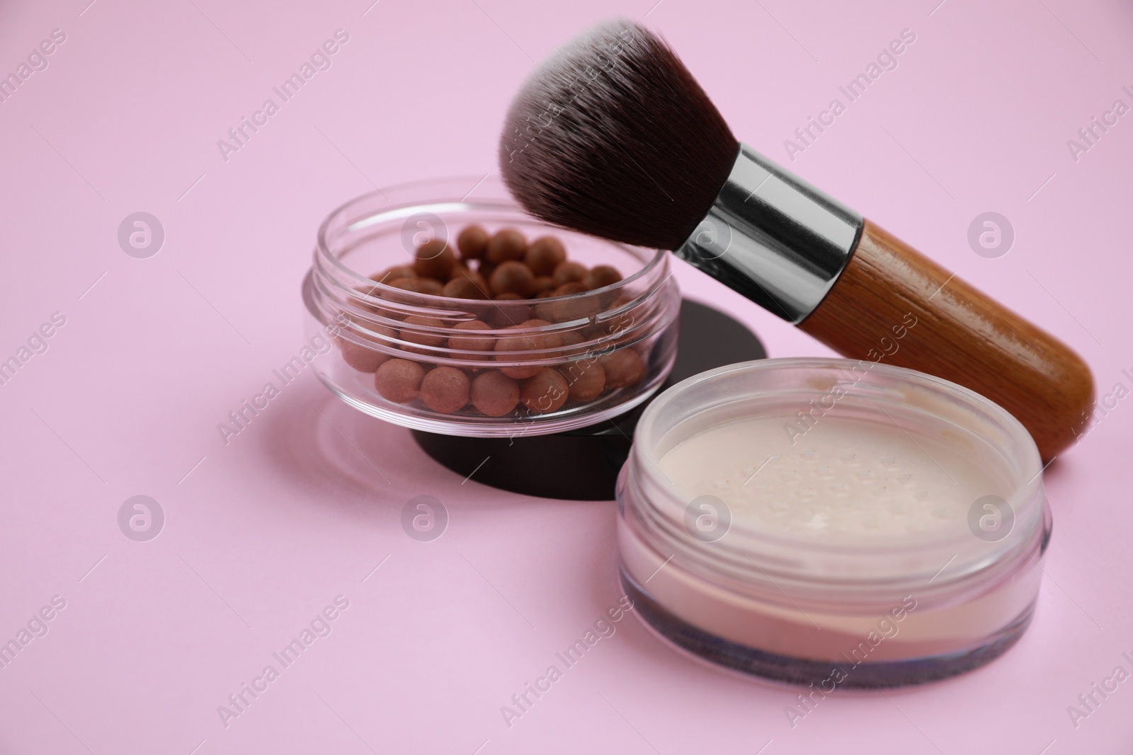 Photo of Different face powders and brush on pink background, closeup