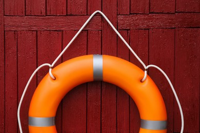 Orange life buoy hanging on red wooden wall