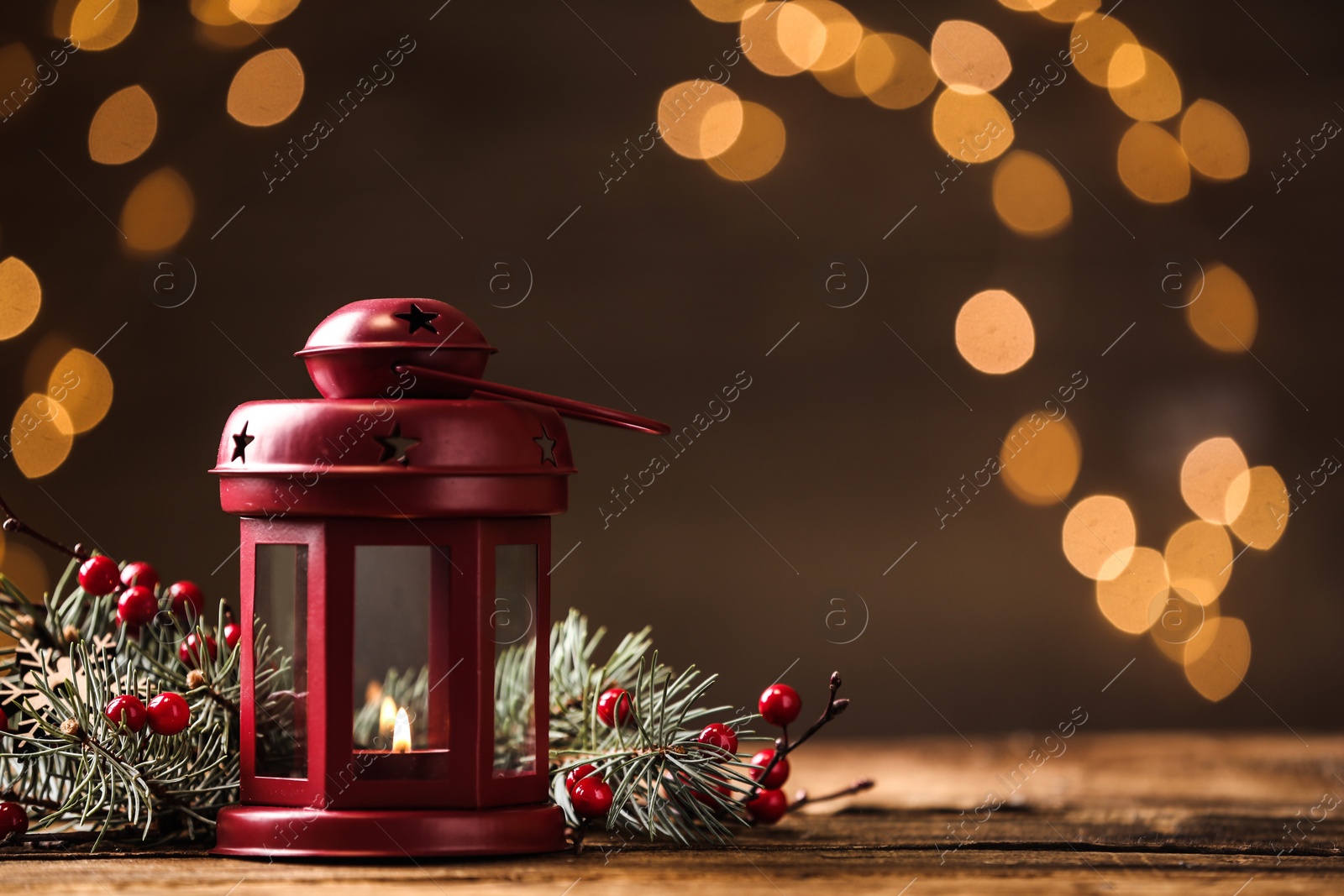 Photo of Lantern and Christmas decor on wooden table against blurred festive lights, space for text. Winter holiday