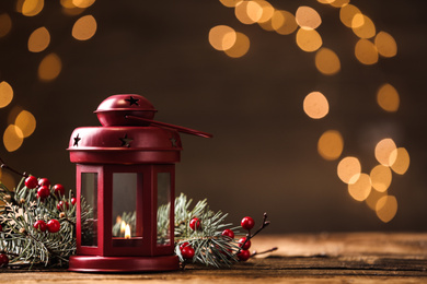 Photo of Lantern and Christmas decor on wooden table against blurred festive lights, space for text. Winter holiday