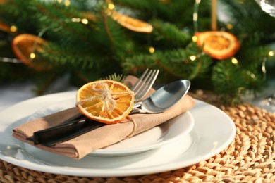 Festive place setting with beautiful dishware, fabric napkin and dried orange slice for Christmas dinner on table, closeup