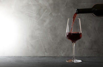 Photo of Pouring red wine from bottle into glass on table. Space for text