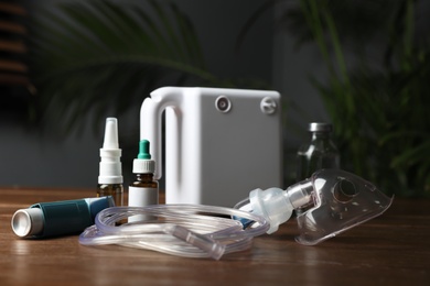 Modern nebulizer with face mask and medications on wooden table indoors. Inhalation equipment