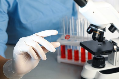 Scientist holding microscope slide with red sample in laboratory, closeup