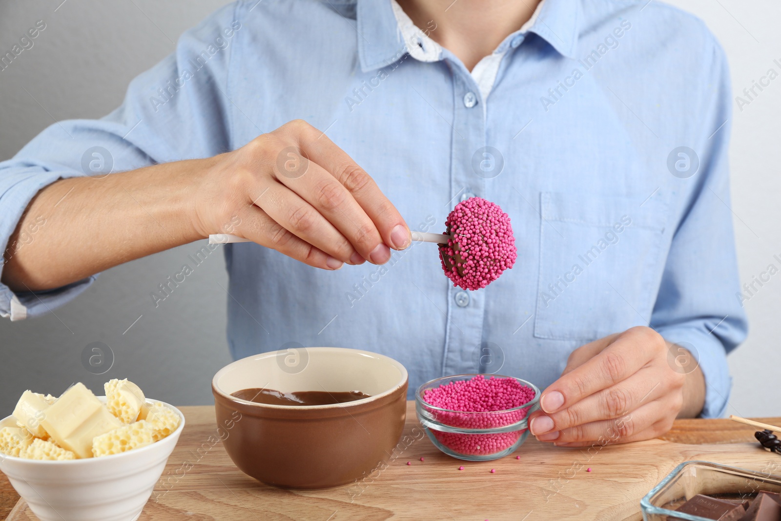 Photo of Young woman with cake pop in pink sprinkles on wooden board, closeup