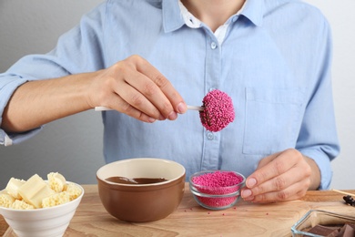 Young woman with cake pop in pink sprinkles on wooden board, closeup