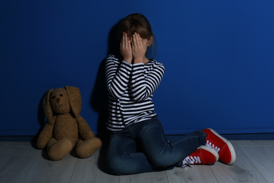 Abused little girl crying near blue wall. Domestic violence concept