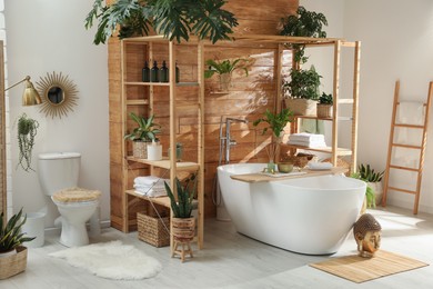 Stylish bathroom interior with white tub and green houseplants near wooden wall. Idea for design