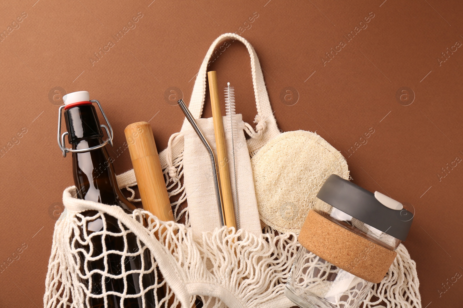 Photo of Fishnet bag with different items on brown background, top view. Conscious consumption