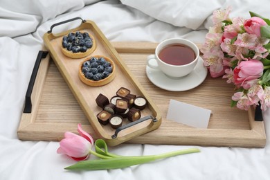 Photo of Tasty breakfast served in bed. Delicious desserts, tea, flowers and blank card on tray