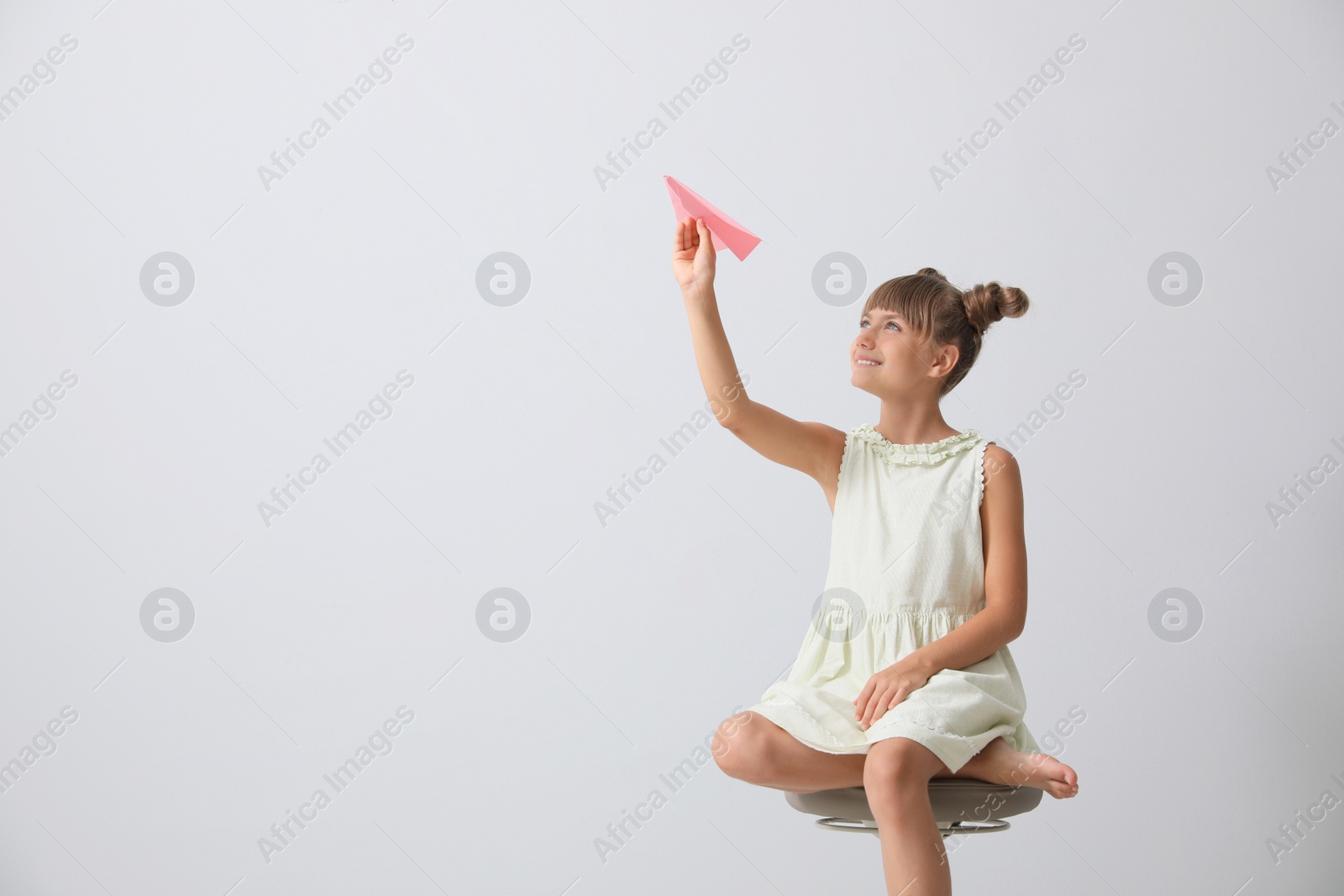 Photo of Cute little girl playing with paper plane on light grey background. Space for text