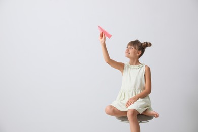 Cute little girl playing with paper plane on light grey background. Space for text