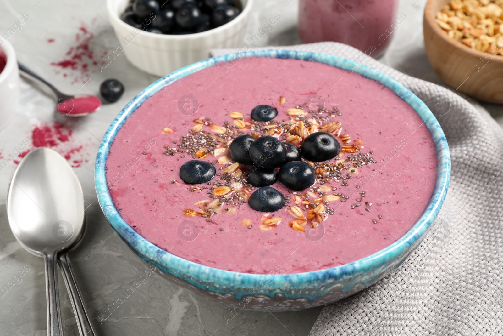 Photo of Delicious acai smoothie with granola and chia seeds served on grey  table, closeup