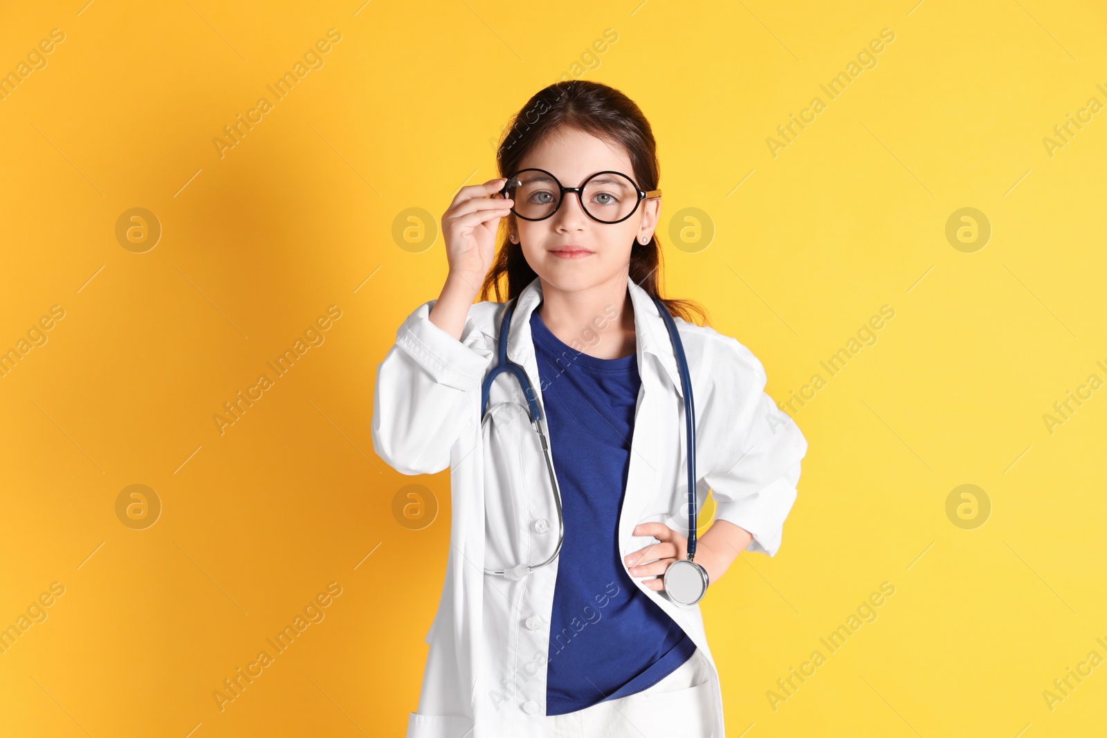 Photo of Little girl with eyeglasses and stethoscope dressed as doctor on yellow  background. Pediatrician practice